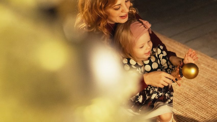 Tender moment between mother and daughter decorating a festive Christmas tree.