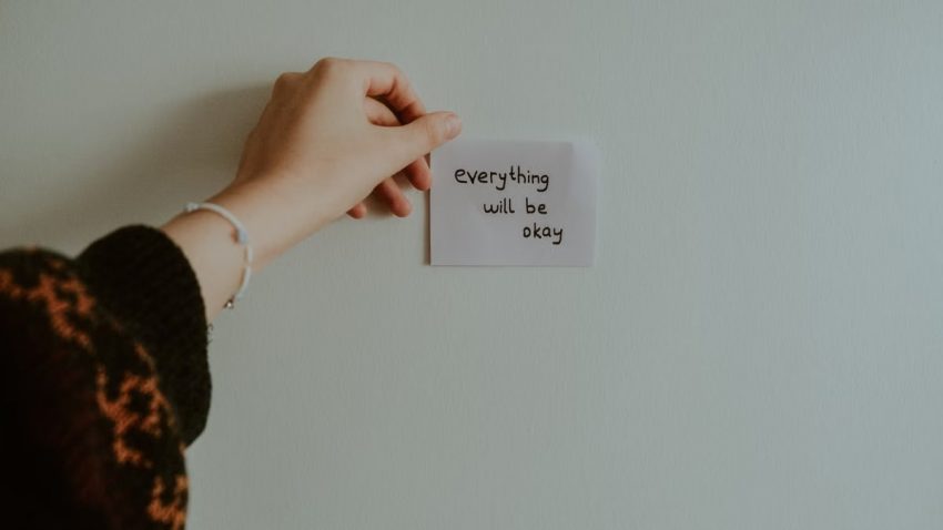 A hand holding a motivational note with uplifting text in an indoor setting.